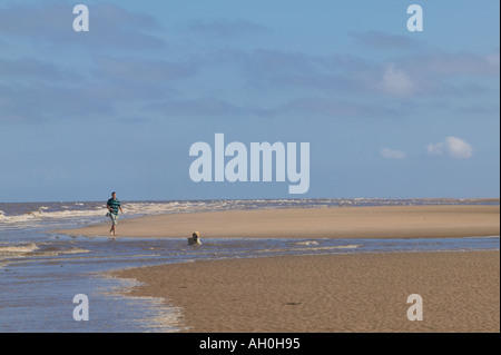 Mann zu Fuß golden Retriever Hund entlang der Kante des ankommenden Meeres Formby Merseyside Stockfoto