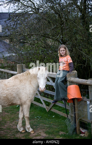 Kaukasische Mädchen sitzen auf Zaun mit weißen Welsh Mountain Pony Stockfoto