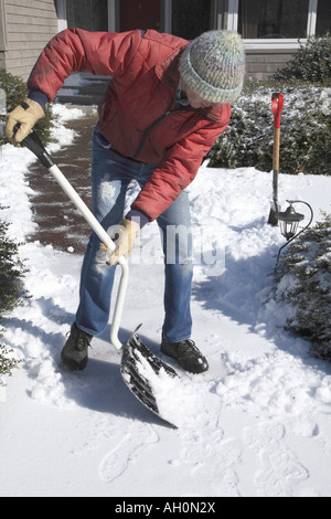 Mann beugte sich über und rechts mit gebogenen behandelt Schneeschaufel Schaben dünne Schicht Schnee von den Weg auf der rechten Seite Stockfoto