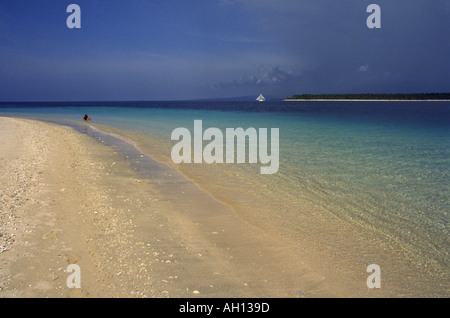 Heftige Regenwolken sammeln sich auf den Gili-Inseln vor Lombok, Indonesien, mit einer alleinstehenden Frau im Wasser und einem segelboot in der Ferne. Stockfoto