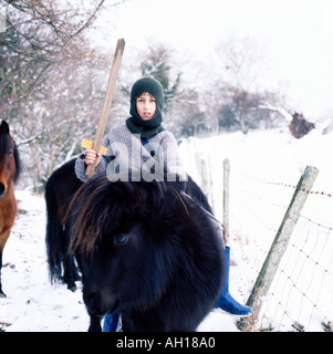 Knabe Kind trägt eine Balaclava sitzt auf einem Pferd halten Ein hölzernes Schwert in schneebedeckten ländlichen Landschaft Carmarthenshire WALES GROSSBRITANNIEN KATHY DEWITT Stockfoto