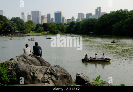 Junges Paar Blick auf Central Park Lake mit Bootsfahrer und Skyline von New York City, Manhattan Stockfoto