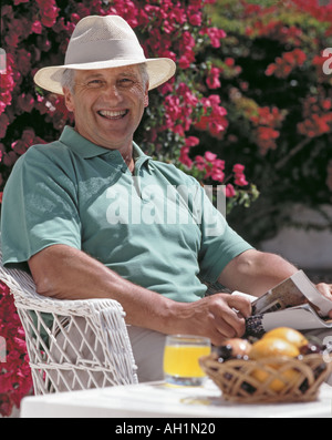 ehemaliger Alter Mann sonnte sich auf Gartenterrasse und Fruchtsaft Stockfoto