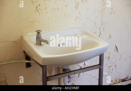 Ein Waschbecken mit Pushdown Tap und kleinen Stück Seife in einem heruntergekommenen Zimmer mit stark abblätternde cremefarbenen Wänden Nahaufnahme Stockfoto