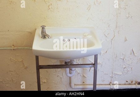 Ein Waschbecken mit Pushdown Tap und kleinen Stück Seife in einem heruntergekommenen Zimmer mit stark abblätternde cremefarbenen Wänden Nahaufnahme Stockfoto