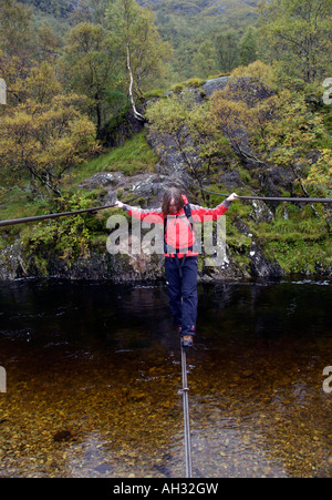 Weibliche Trekker Überquerung einer Hängebrücke in Glen Nevis, Schottland Stockfoto