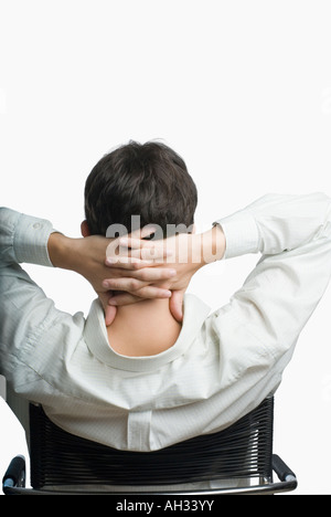 Rückansicht der ein junger Mann sitzt auf einem Sessel mit den Händen hinter dem Kopf Stockfoto