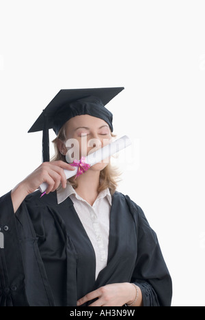 Junge Frau trägt ein Kleid Graduierung und küssen ihr Diplom Stockfoto