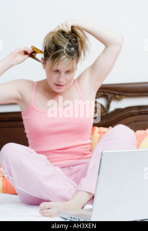 Junge Frau sitzt vor einem Laptop und binden ihre Haare Stockfoto