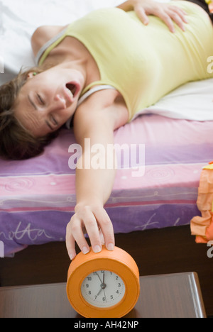 Erhöhte Ansicht einer jungen Frau auf dem Bett liegend und erreichen für einen Wecker Stockfoto