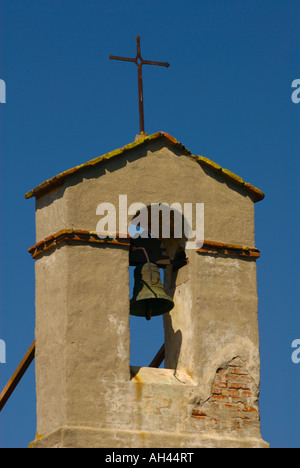 Einem schmiedeeisernen Kreuz auf dem Backstein und Adobe Glockenturm gegen einen klaren blauen Himmel in der Mission San Juan Capistrano, CA, USA Stockfoto