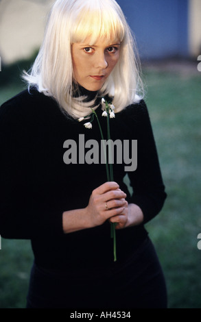 Platin blonde weiblich gekleidet in schwarzen lange Stielen von Schneeglöckchen Blumen in ihren Händen hält Stockfoto