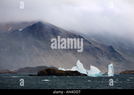 Dramatische Berge unter niedrigen grauen Himmel mit gezackten weißen Eisberge und schwarzen Felsen im Meer vor der südwestlichen Küste von Grönland Stockfoto