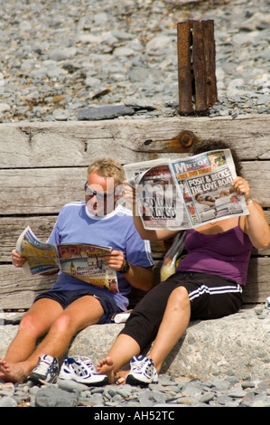 Ehepaar, Mann und Frau sitzen am Strand lesen Sonntag Boulevardzeitungen, Aberystwyth Ceredigion Wales UK Stockfoto