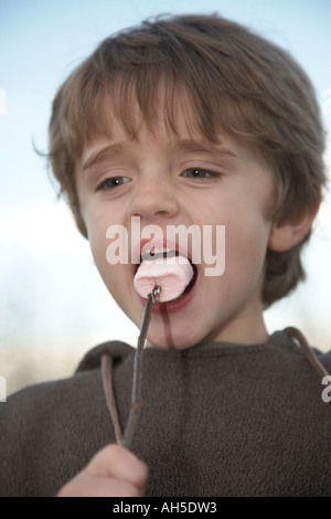 Kind, Rösten Marshmallows im Garten draußen und Essen aus einem stick Stockfoto