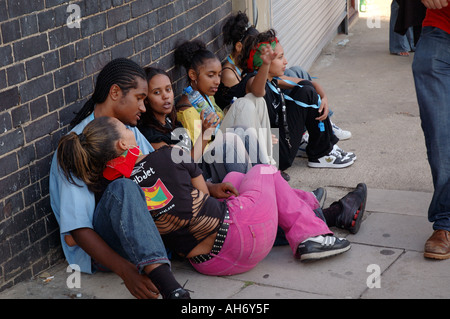Gruppe von Jugendlichen sitzen auf Bürgersteig wartenden ausruhen, Chillen am Notting Hill Carnival. Stockfoto