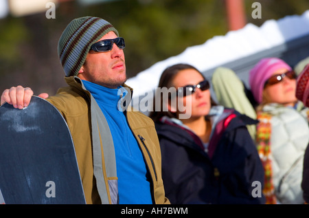 Mitte erwachsenen Mann, der ein Snowboard mit zwei Frauen hinter ihm hält Stockfoto