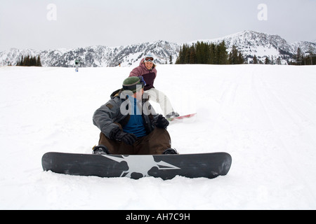 Mitte erwachsenen Mann sitzt auf Schnee mit einer Mitte erwachsenen Frau hinter ihm gleiten Stockfoto