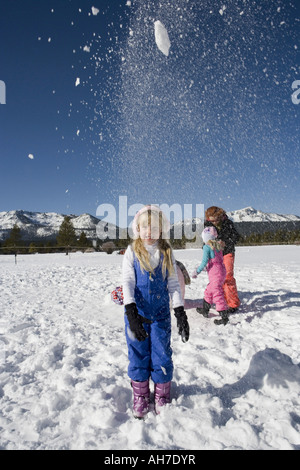 Mädchen werfen Schnee mit ihrer Mutter und Schwester im Hintergrund Stockfoto