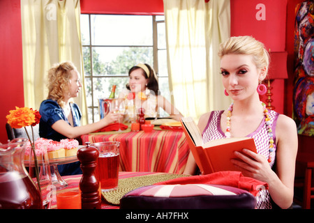 Junge Frau hält ein Buch mit zwei jungen Frauen Essen in einem Restaurant hinter ihr Stockfoto