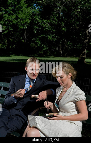 Junges Paar auf einer Parkbank sitzen und Sushi-Essen Stockfoto