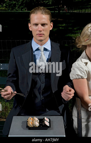 Junger Mann mit einer jungen Frau auf einer Parkbank sitzen und Sushi-Essen Stockfoto