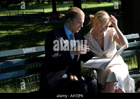 Unternehmer und Unternehmerin sitzt auf einer Parkbank, Blick auf einen laptop Stockfoto