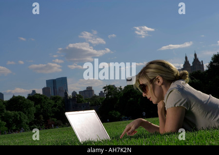 Junge Frau liegend vor einem Laptop in einem Park, New York City, New York, USA Stockfoto