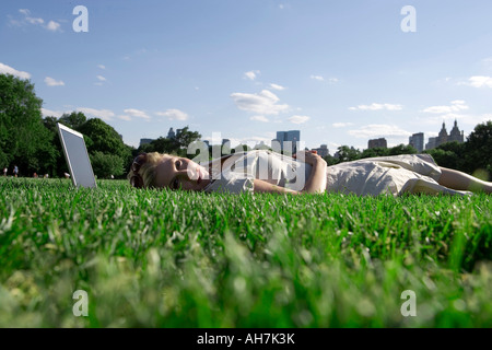 Junge Frau liegend in einem Park mit einem Laptop unter dem Kopf Stockfoto
