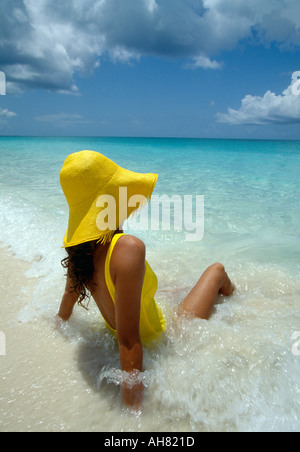 Turks und Caicos Provo-Frau im gelben Hut und gelben Anzug sitzt im Meeresbrandung Stockfoto