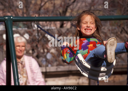Lachen und spielen Mädchen auf Schaukel mit ihrer Großmutter drücken Stockfoto