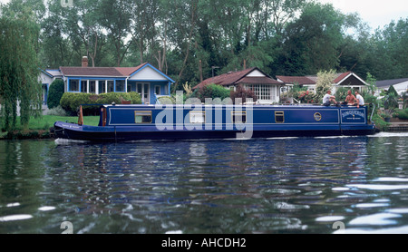 Traditionellen Narrowboat auf der Themse vorbei am Fluss auf dem Land, mit drei Männern am Heck, Shepperton, Surrey, England Stockfoto