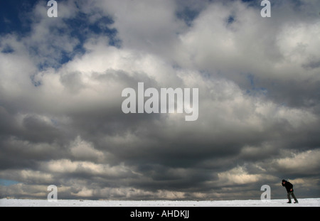 Ein Mann geht über den Schnee bei bewölktem Himmel auf der South Downs Way in der Nähe von Brighton in Südengland Stockfoto