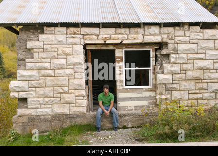 Ein Hispanic Mann in einem grünen Hemd sitzt ruhig in das leere Tor der verfallenen Ruinen eines Gebäudes Stockfoto