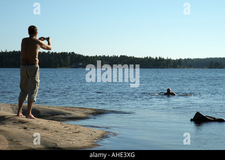 Mann mit einer kompakten Digitalkamera ein Foto seines Freundes Schwimmen im Meer in den schwedischen Schären Stockfoto