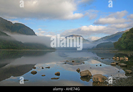 Nebel, Wolken und Reflexionen über Schottland, Loch Lubnaig mit Felsen im Vordergrund.  Blaue Himmel spiegelt sich in dem Loch. Stockfoto