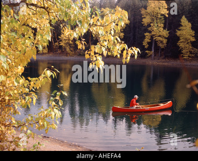 Fischer in einem roten Kanu schwimmt auf den ruhigen Wassern des Scout Lake in Oregon, umrahmt von farbigen Espe Blätter im Herbst Stockfoto