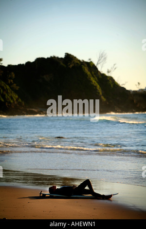 Eine junge Frau entspannt sich nach dem Surfen am Strand von Wategos Byron Bay Australien Stockfoto