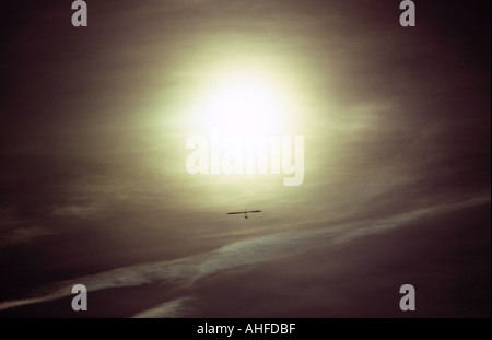 Mann im Hängegleiter im dunklen Himmel fliegen in Richtung Sonne Stockfoto