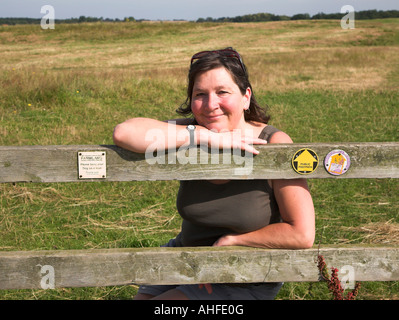 Frau mittleren Alters lächelnd sitzen auf Stil auf Land Fußweg Burrow Hill, Boyton, Suffolk, England, Großbritannien Stockfoto