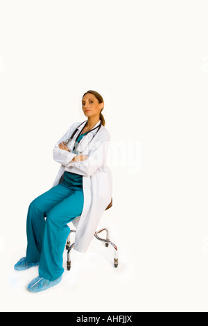 Porträt der Ärztin sitzen auf Stuhl in Scrubs und Lab Wappen gekreuzt Stockfoto