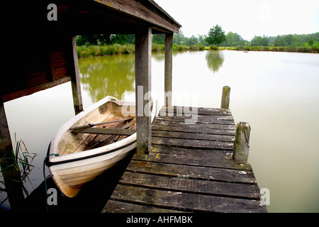 Ruderboot im hölzernen Bootshaus neben Bootssteg am See Landes Stockfoto
