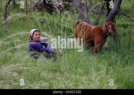 Frau sitzt in den Rasen durch die am Straßenrand Pflege und Weiden ihre Ziege im südlichen türkischen Hilltown village.nomadic Stockfoto