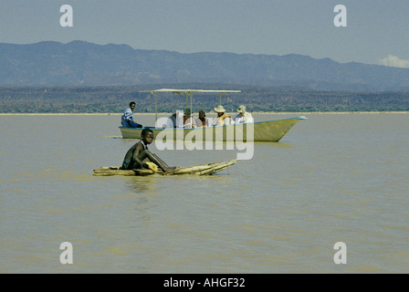 Touristen in ein Motorboot in der Nähe von Njemps junge reitet auf seinem Ambach Kanu am Lake Baringo im Great Rift Valley Kenia Osten Stockfoto