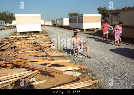 Mann sitzt in der Sonne lesen Zeitung außerhalb neben einer abgerissenen statische Wohnwagen bei Trecco Bay Porthcawl South Wales UK Stockfoto