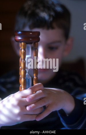 Kleiner Junge beobachten Sandkörner in Sanduhr fallen Stockfoto