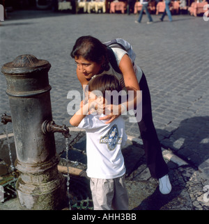 Mutter und Kind an einem öffentlichen Wasserhahn zum Trinken und Waschen der Hände, die vor der Straße am Pantheon in Rom, Italien, STEHEN, KATHY DEWITT