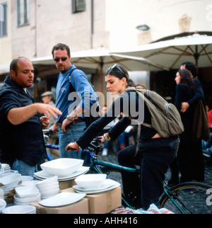 Eine schöne Radfahrerin auf einem Fahrrad beim Stöbern Geschirr Teller Und Bowls auf einem Marktstand in der Nähe von Campo dei Fiori Straßenmarkt in Rom Italien KATHY DEWITT Stockfoto
