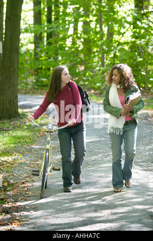 Zwei weibliche College-Studenten auf dem Weg zu einem führt Bücher der Klasse zu sprechen und man geht ein Fahrrad Stockfoto