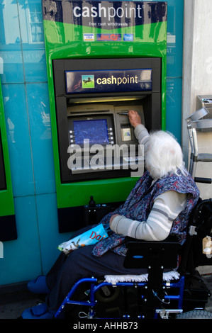 Älterer Rollstuhlfahrer Bargeld von Lloyds Bank Cashpoint, UK Stockfoto